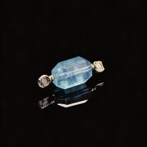 May include: A light blue, faceted gemstone pendant with silver-colored metal accents. The gemstone has a rectangular shape with multiple sides. The pendant is displayed against a black background.
