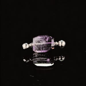 May include: A faceted, purple amethyst gemstone bead with silver-colored metal end caps and spheres. The gemstone is rectangular with a polished, reflective surface. The bead is displayed against a black background.