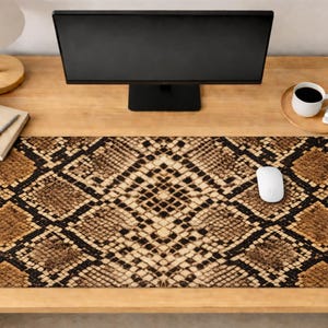 Può includere: Tappetino per scrivania rettangolare con motivo a pelle di serpente nei toni del marrone e del nero. Un mouse per computer bianco è posizionato sul tappetino. Il tappetino è su una scrivania di legno con un monitor, una lampada e una tazza di caffè.