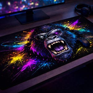 May include: Black rectangular mouse mat featuring a vibrant, colourful illustration of an angry gorilla with an open mouth. The gorilla's fur is dark blue and purple, with bright yellow, pink, and blue paint splashes. A computer mouse is visible on the right.