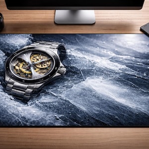 May include: A silver wristwatch with a detailed, exposed movement sits on a large mousepad with a blue and white abstract design. The watch has a silver band and a black bezel. Other items on the wooden desk include a black notebook, pen, headphones, phone, and a white mouse.