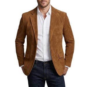 Può includere: Una giacca in camoscio marrone con chiusura a due bottoni, abbinata a una camicia bianca e jeans blu scuro. La giacca ha due tasche frontali e un revers a lancia. L'outfit ha un aspetto casual ma sofisticato.