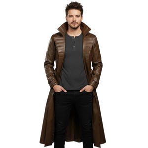 May include: A brown leather trench coat with a wide collar and buttoned cuffs. The coat is long, reaching the ankles, and has a tailored fit. The model is wearing a gray Henley shirt and black pants.