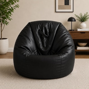 May include: A large, black leather bean bag chair. The chair has a rounded shape and a handle at the top. The bean bag is placed on a light-coloured rug.