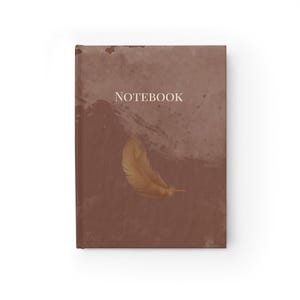 Könnte beinhalten: Ein Notizbuch mit braunem Einband und dem weißen Wort „NOTEBOOK“. Auf dem Einband ist eine goldene Feder abgebildet. Das Notizbuch hat einen strukturierten, aquarellartigen Hintergrund.