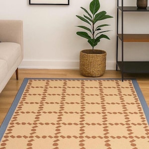Puede incluir: Alfombra rectangular con estampado geom&eacute;trico beige y marr&oacute;n y borde azul. El dise&ntilde;o de la alfombra consiste en formas marrones repetidas sobre un fondo beige. Est&aacute; colocada sobre un suelo de madera.