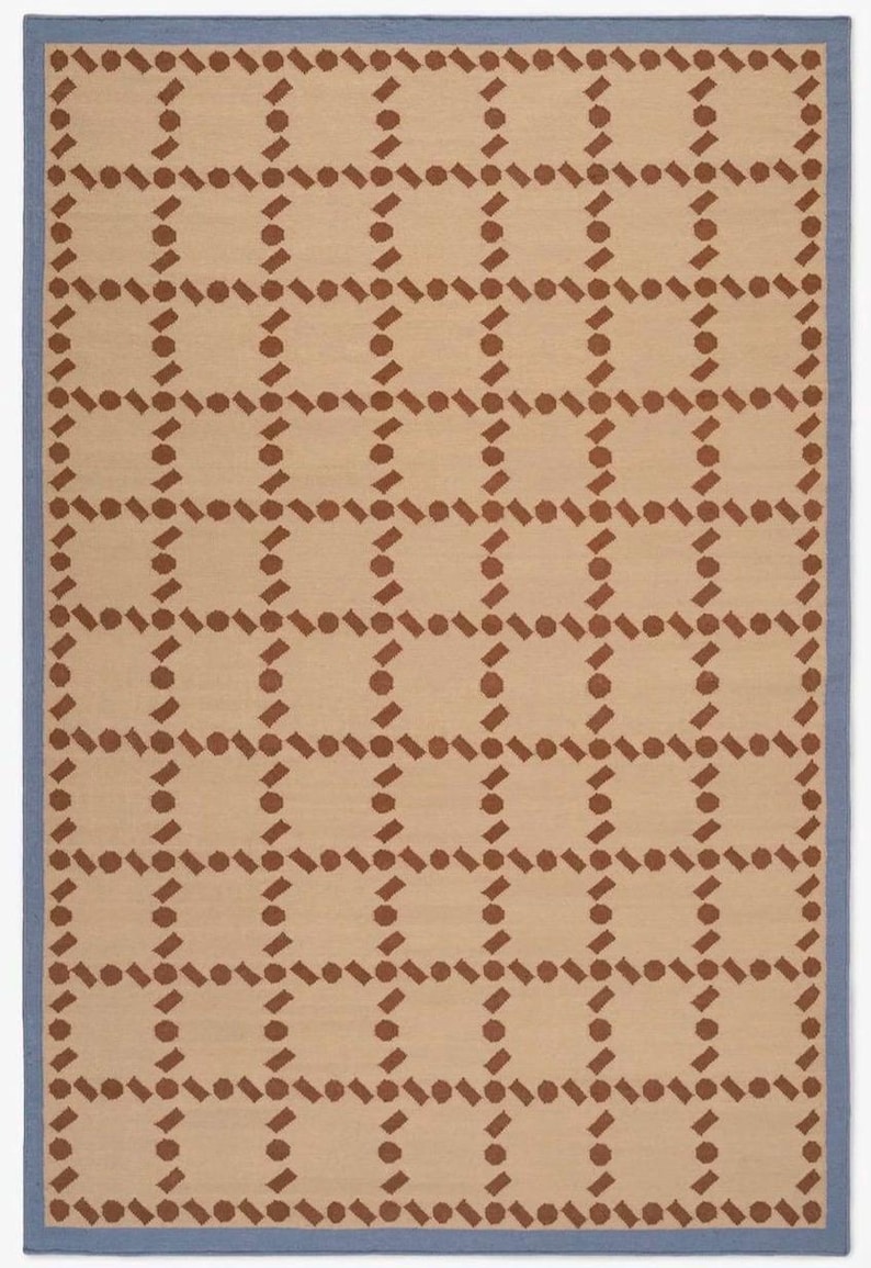 Puede incluir: Alfombra rectangular con un patr&oacute;n geom&eacute;trico repetitivo. La alfombra presenta un fondo beige con una cuadr&iacute;cula de formas marrones y un borde azul. El dise&ntilde;o es sim&eacute;trico y moderno.