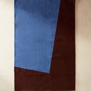 Op de afbeelding: Rechthoekig vloerkleed met een geometrisch ontwerp. Het vloerkleed heeft een groot blauw gedeelte aan de linkerkant en een donkerbruin gedeelte aan de rechterkant. Het vloerkleed is gemaakt van geweven materiaal.