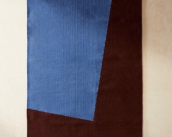 Op de afbeelding: Rechthoekig vloerkleed met een geometrisch ontwerp. Het vloerkleed heeft een groot blauw gedeelte aan de linkerkant en een donkerbruin gedeelte aan de rechterkant. Het vloerkleed is gemaakt van geweven materiaal.