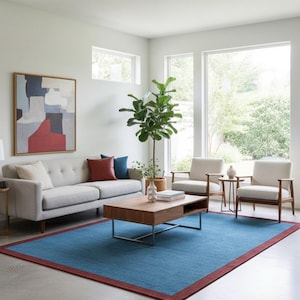 Puede incluir: Un sal&oacute;n moderno con un sof&aacute; gris claro, dos sillones y una mesa de centro de madera. Una gran alfombra azul con un borde rojo cubre el suelo. Una gran pintura abstracta cuelga de la pared y una planta alta est&aacute; en la esquina.