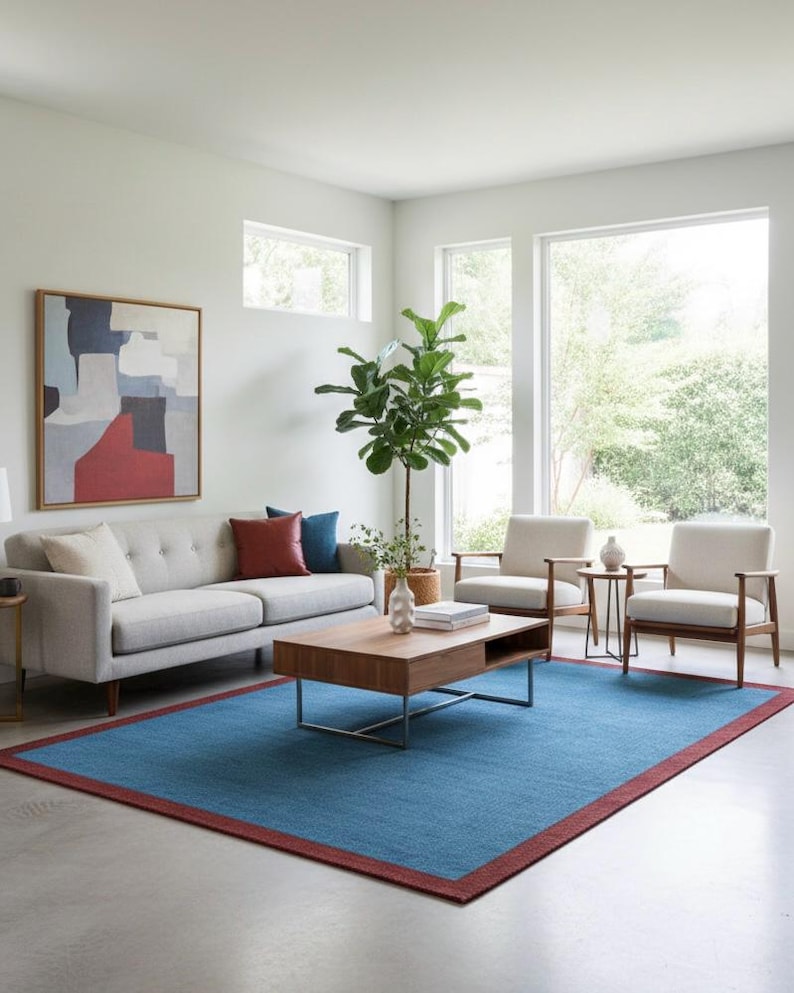 Puede incluir: Un sal&oacute;n moderno con un sof&aacute; gris claro, dos sillones y una mesa de centro de madera. Una gran alfombra azul con un borde rojo cubre el suelo. Una gran pintura abstracta cuelga de la pared y una planta alta est&aacute; en la esquina.
