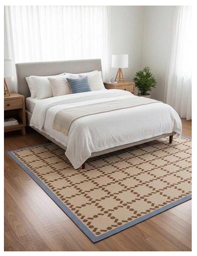 Puede incluir: Una habitaci&oacute;n con una cama con ropa de cama blanca, almohadas y un cabecero gris. Una alfombra estampada con un borde azul y una mesita de noche de madera con una l&aacute;mpara est&aacute;n en la habitaci&oacute;n. Una peque&ntilde;a planta est&aacute; en la mesita de noche.