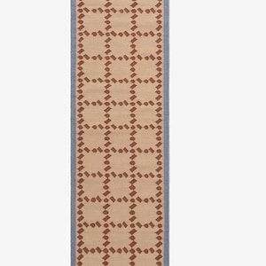 Puede incluir: Una alfombra rectangular beige con un patr&oacute;n geom&eacute;trico repetitivo en marr&oacute;n. La alfombra tiene un borde azul. El patr&oacute;n consiste en cuadrados y puntos. Esta alfombra es adecuada para un pasillo o entrada.