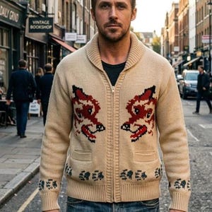 Peut inclure: Un gilet zippé en tricot beige avec un col châle, deux poches avant et un motif répété de têtes de renard rouges sur la poitrine, accompagné de motifs d'empreintes de pattes bleu foncé sur l'ourlet inférieur et les poignets, porté sur un t-shirt noir.