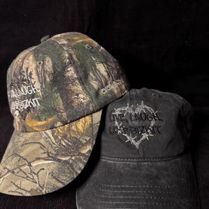 May include: Two baseball caps. One is camouflage with the text "LIVE LAUGH LIMP BIZKIT" embroidered in white. The other is black with the same text and a barbed wire design, also embroidered in white.