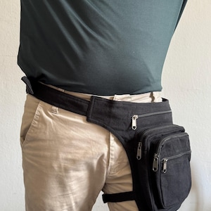 Pode incluir: Uma bolsa de perna em lona preta com uma alça larga de cintura e uma alça de coxa ajustável. A bolsa inclui um compartimento superior com fecho horizontal e um bolso frontal maior com duas secções verticais com fecho.