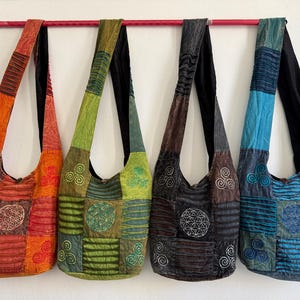 Puede incluir: Cuatro bolsos de hombro estilo hobo hechos de tela de patchwork, cada uno con una correa larga, un patrón geométrico circular central y motivos de espiral más pequeños. Los bolsos se presentan en colores naranja, verde, marrón oscuro y azul.
