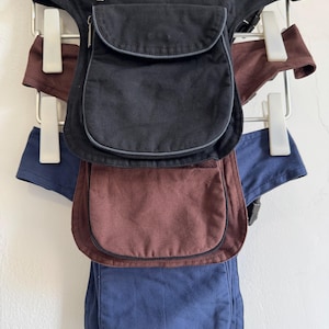 May include: Three leg bags featuring a top zippered compartment and a larger main pocket with a flap closure. The bags are available in black, brown, and blue, each equipped with adjustable straps and buckles for secure attachment around the leg.