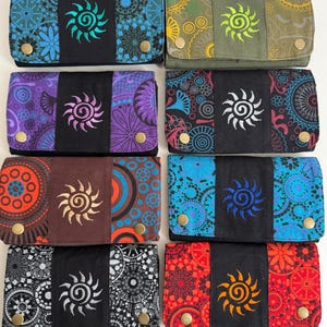 May include: Eight rectangular fabric wallets arranged in two columns, each featuring a central black panel with an embroidered sun design, flanked by patterned side panels in various colours including blue, purple, red, green, and orange.