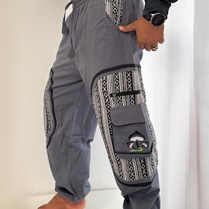Op de afbeelding: Grijze cargobroek met een elastische tailleband met trekkoord, zijzakken en zwart-wit patroonstofpanelen. De broek heeft een klepzak aan de zijkant die is versierd met een geborduurd paddenstoelontwerp als grafische afbeelding.