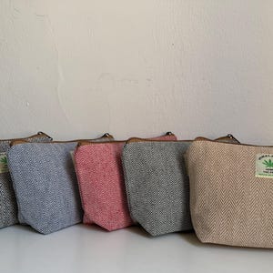 Op de afbeelding: Vijf ritszakjes op een rij, elk met een geweven visgraatpatroon in zwart, blauw, rood, donkergrijs en beige. Elk zakje heeft een klein rechthoekig label met een groen bladicoon en de tekst HIMALAYAN HEMP THC FREE.
