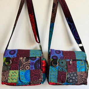 Può includere: Due borse a tracolla patchwork colorate con cinghie regolabili. Le borse presentano una varietà di quadrati di tessuto fantasia nei toni del blu, viola, verde e rosso. Ogni borsa ha una tasca frontale e una chiusura con cerniera.