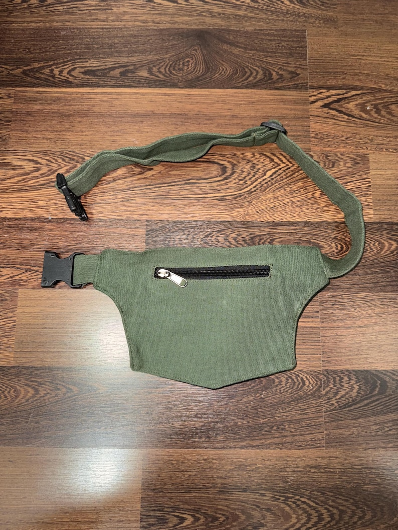 May include: An olive green fanny pack with a black zipper and adjustable strap. The pack has a rectangular shape with a curved bottom and a black plastic buckle closure. The strap is made of the same olive green material.