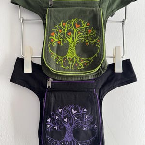 May include: Two utility hip bags, one olive green and one black, each featuring a zipped top pocket and a flap-covered main compartment. Both bags display a screen-printed tree of life design with small heart-shaped leaves in contrasting colours.