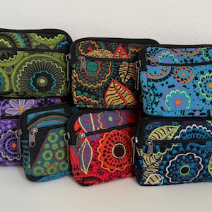 Op de afbeelding: Een verzameling kleine, rechthoekige stoffen etuis met vakken met ritssluiting. Elke etui heeft een uniek, kleurrijk bloemen- of abstract patroon in groen, blauw, paars, rood en oranje. De etuis hebben zwarte ritsen en afwerking.
