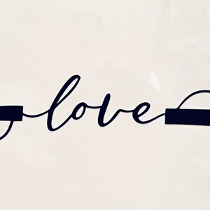 May include: A black cursive "love" word art design. The word is flanked by two dark rectangular shapes with curved lines extending from each end. The design is set against a white background.