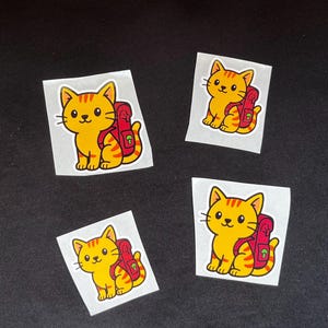 Puede incluir: Cuatro pegatinas con un gato de dibujos animados con cuerpo amarillo y rayas naranjas. El gato lleva una mochila roja. Las pegatinas est&aacute;n sobre un fondo blanco, sobre un fondo negro.