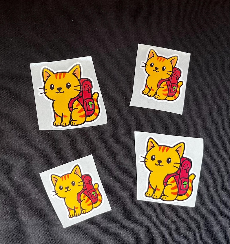 Puede incluir: Cuatro pegatinas con un gato de dibujos animados con cuerpo amarillo y rayas naranjas. El gato lleva una mochila roja. Las pegatinas est&aacute;n sobre un fondo blanco, sobre un fondo negro.