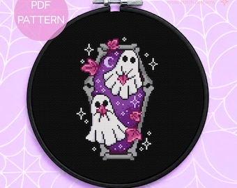 Puede incluir: Un patrón de punto de cruz en un bastidor negro con dos fantasmas blancos dentro de una forma de ataúd morado sobre tela negra. El diseño incluye hojas rosas, una luna creciente y estrellas blancas. El texto dice PDF PATTERN y Enchanted Peach Pixels.