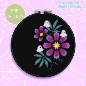 May include: A black embroidery hoop containing a cross stitch pattern on black fabric. The design features two purple flowers with yellow centers, teal green leaves, and three small white ghost figures. Text in the image reads PDF PATTERN and Enchanted Peach Pixels cross stitch patterns.