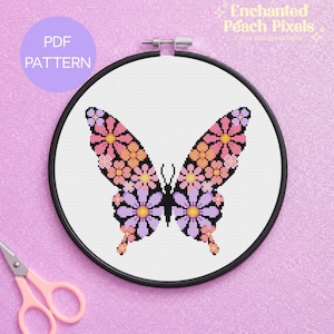 May include: A cross stitch pattern featuring a butterfly design composed of pink, orange, and purple flowers on a white fabric background, held within a black circular embroidery hoop. The text Enchanted Peach Pixels cross stitch patterns is visible.