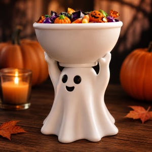 May include: A white ceramic bowl held up by a ghost-shaped base with black eyes and a smiling mouth. The bowl is filled with assorted colorful Halloween candies, including small orange pumpkins, candy corn, and various wrapped sweets.