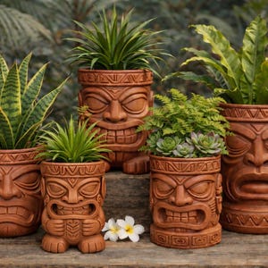 Può includere: Cinque fioriere tiki in ceramica marrone di varie dimensioni, ciascuna con un design a volto scolpito. Le fioriere contengono piante verdi, tra cui piante del serpente e felci. Due piccoli fiori bianchi sono davanti.