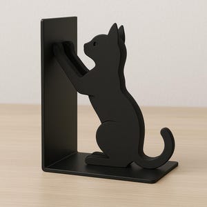 Peut inclure: Un serre-livres noir en métal en forme de chat. Le chat est assis, ses pattes tendues pour tenir un livre. Le serre-livres a une base rectangulaire et un support vertical. La silhouette du chat est détaillée.