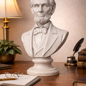 Puede incluir: Busto detallado de Abraham Lincoln, esculpido en un tono claro y neutro. La escultura presenta una pajarita y un traje formal. El busto se exhibe sobre un escritorio de madera, junto a libros, una lámpara e instrumentos de escritura.