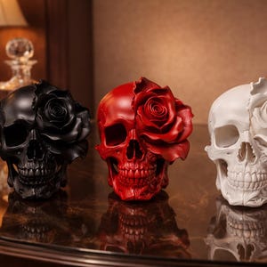 Puede incluir: Tres esculturas decorativas de calaveras, cada una con una rosa floreciendo de un lado. Las calaveras son negras, rojas y blancas. Las esculturas están sobre una superficie reflectante.