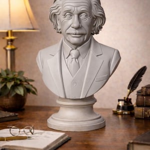 Peut inclure: Buste gris clair d'Albert Einstein, sculpté avec des traits du visage détaillés, dont ses cheveux et sa moustache emblématiques. Le buste est sur un socle, et porte un costume et une cravate. Le buste est exposé sur un bureau en bois.
