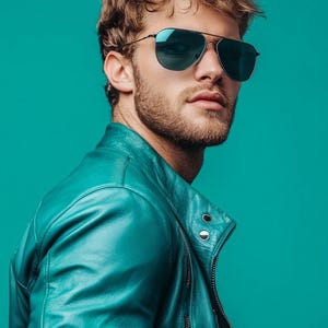May include: A person wearing aviator sunglasses with a dark teal tint and a teal leather jacket. The sunglasses have a thin, dark metal frame. The jacket has a zipper closure and a classic biker style. The background is a solid teal color.