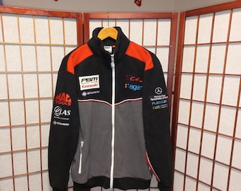 May include: Black, gray, and orange racing jacket with multiple sponsor logos. The jacket has a full-length zipper, a stand-up collar, and a gray lower section. Logos include "MAC TOOLS", "PBM Kawasaki", and "C4 Lager".