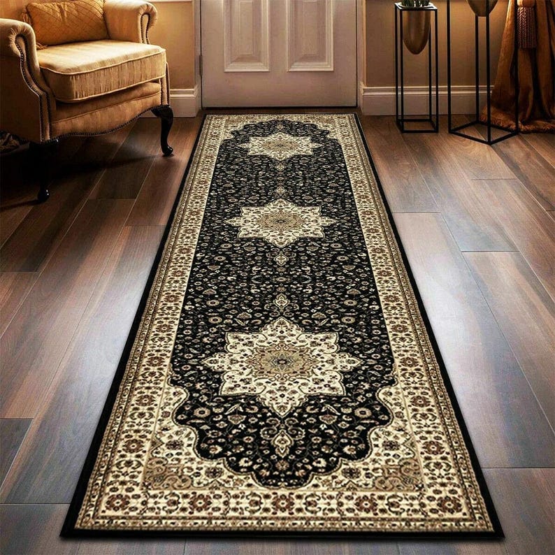 May include: A long, rectangular black rug with an ornate beige and brown floral pattern. The rug features a central design with repeating star-like medallions and a detailed border, suitable for a hallway or entryway.