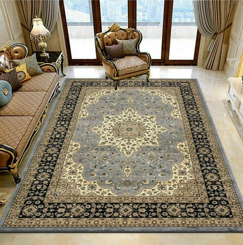 May include: A large, rectangular area rug with an ornate floral design. The rug features a central medallion in cream and beige, surrounded by a light blue field. A black and brown border frames the rug, adding a touch of elegance to the room.