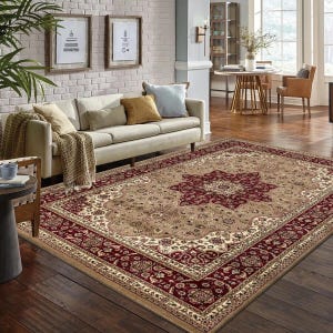 May include: A large, rectangular area rug with an ornate, traditional design. The rug features a central medallion in deep red, surrounded by a beige field and a red border. The rug is placed in a living room setting with a sofa and decorative pillows.