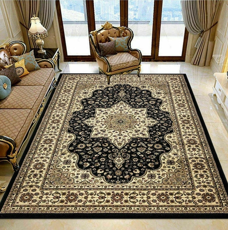 May include: A rectangular area rug with an ornate floral pattern. The rug features a central medallion in cream and gold, surrounded by a black field. The border is cream and brown with floral motifs. The rug is placed in a living room setting.