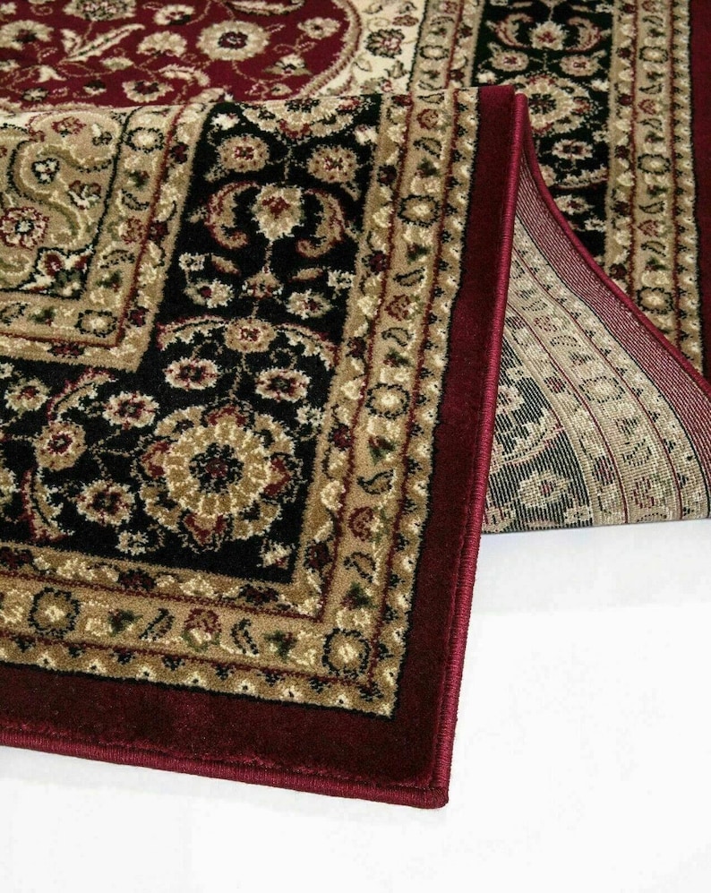 May include: Close-up of a rolled-up area rug with a traditional floral pattern. The rug features a deep burgundy border and a central design in black, beige, and burgundy. The intricate details and color palette create a classic aesthetic.