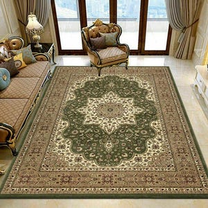 May include: A large, rectangular area rug with an ornate, floral design. The rug features a central medallion in cream and beige, surrounded by a dark green field and a border in shades of brown and green. The rug is placed in a living room setting.