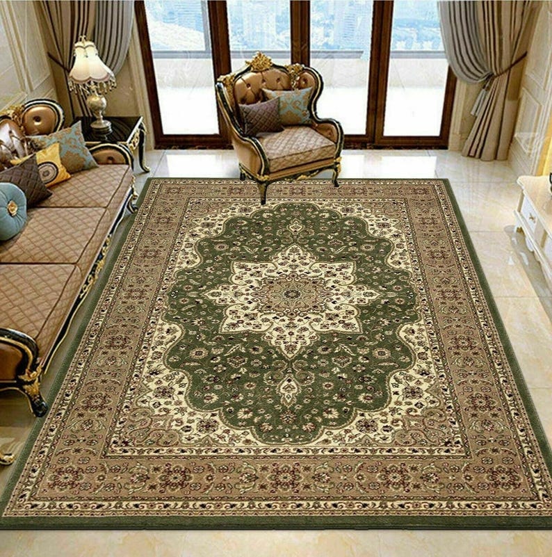 May include: A large, rectangular area rug with an ornate, floral design. The rug features a central medallion in cream and beige, surrounded by a dark green field and a border in shades of brown and green. The rug is placed in a living room setting.